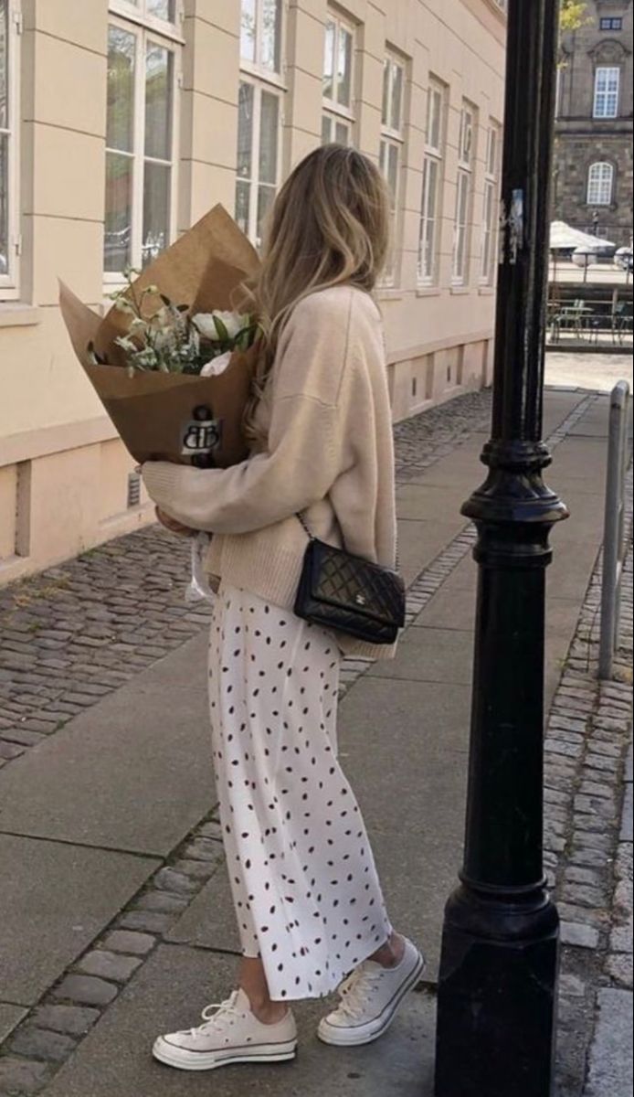woman holding a bundle of flowers wearing an oversized sweater and polka dot skirt.