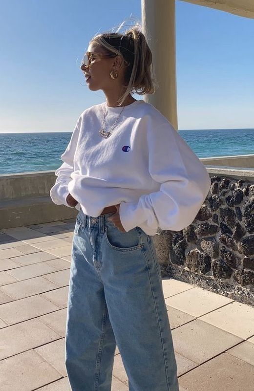 woman wearing baggy mom jeans and a white champion sweatshirt looking into the sun