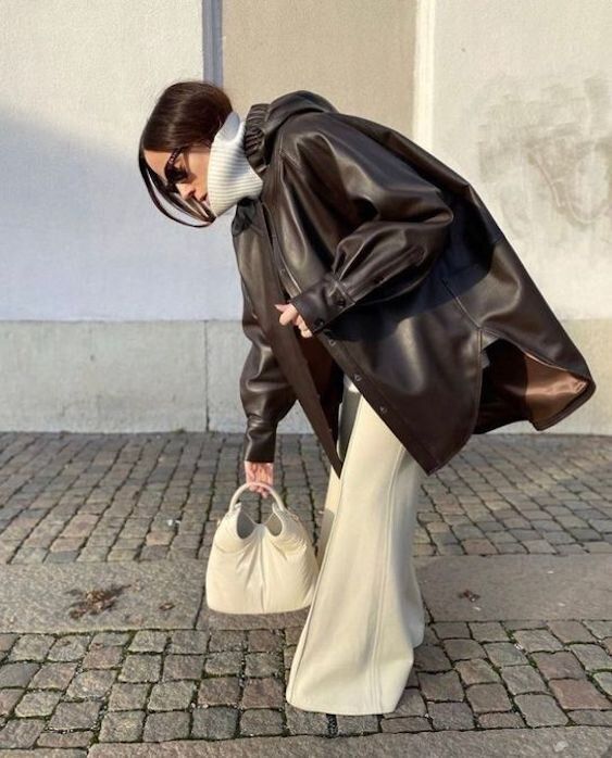 woman wearing a winter outfit with a faux leather jacket, cream pants, sunglasses, and carrying a beige bag