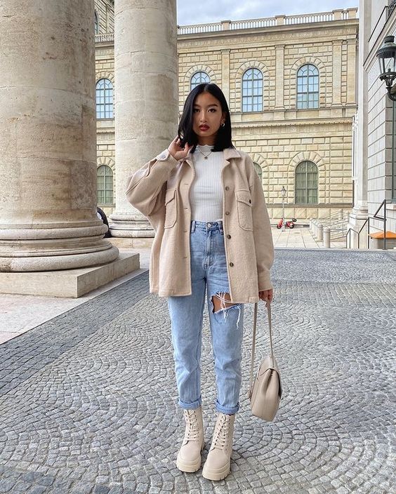 woman standing in Europe wearing a cream shacket, ripped jeans, and cream combat boots