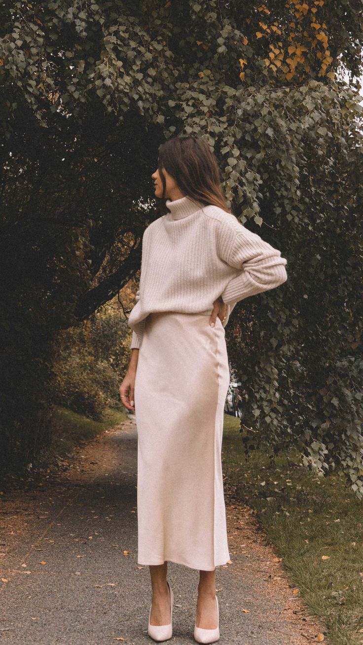 woman wearing a beige silky skirt and a cropped turtleneck sweater outside.