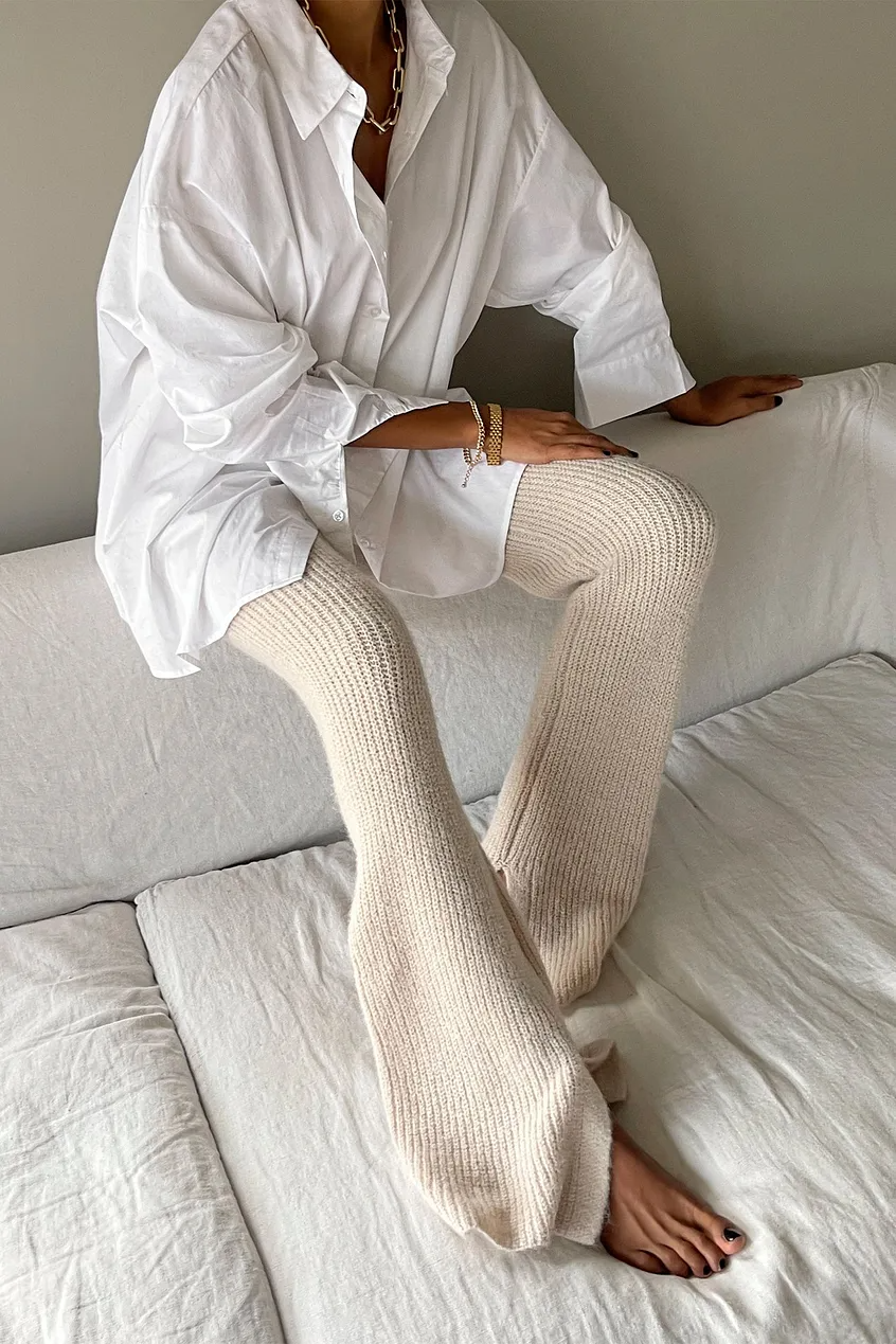 woman sitting on a sofa wearing comfy casual kit pants and an oversized white button up.